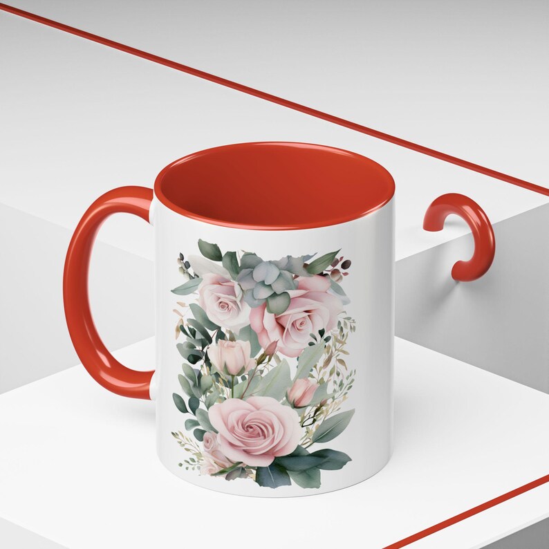 May include: A white ceramic mug with a red rim and handle. The mug features a floral design with pink roses and green leaves.