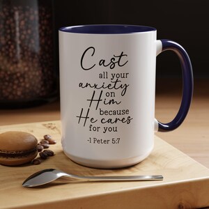 May include: White ceramic coffee mug with a blue rim and handle. The mug features a black inspirational quote: "Cast all your anxiety on Him because He cares for you -1 Peter 5:7".