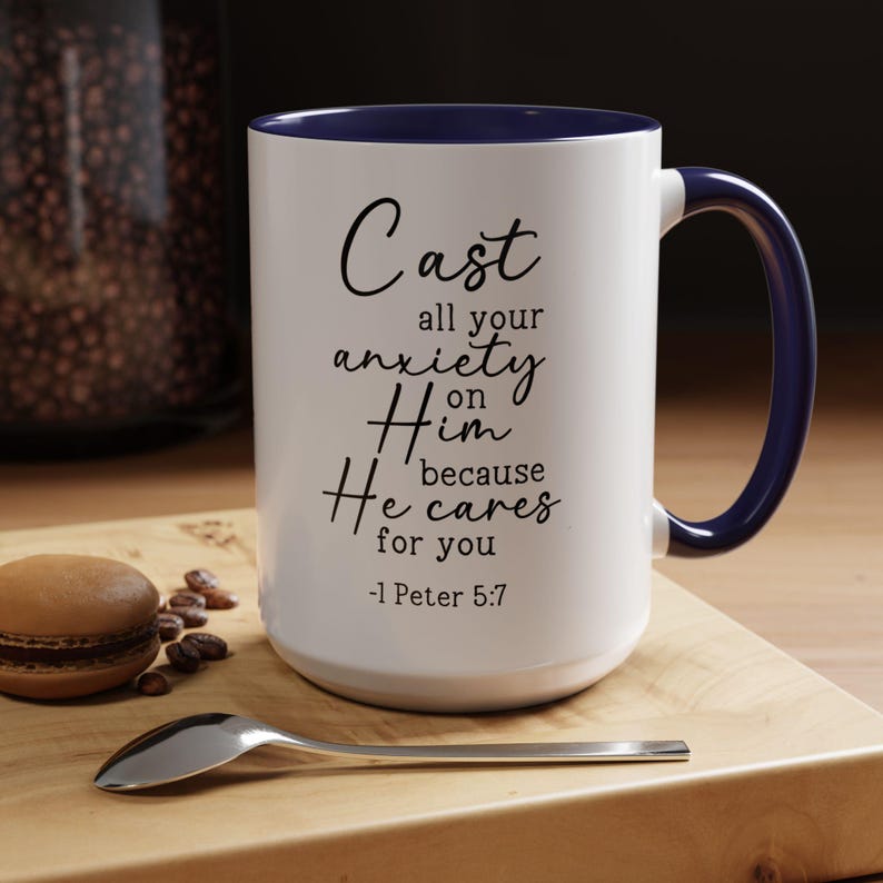 May include: White ceramic coffee mug with a blue rim and handle. The mug features a black inspirational quote: "Cast all your anxiety on Him because He cares for you -1 Peter 5:7".