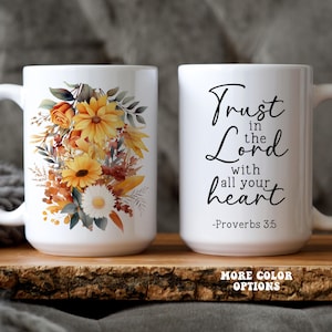 May include: Two white ceramic mugs. One mug features a floral design with sunflowers, roses, and leaves in shades of yellow, orange, and brown. The other mug has the text "Trust in the Lord with all your heart - Proverbs 3:5".