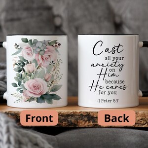 May include: White ceramic mug with a black rim and handle. The front features a floral design with pink roses and green leaves. The back features the text "Cast all your anxiety on Him because He cares for you -1 Peter 5:7".