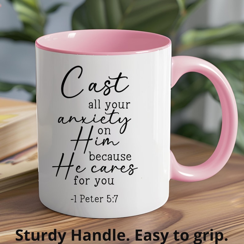 May include: White ceramic coffee mug with a pink rim and handle. The mug has black text that reads "Cast all your anxiety on Him because He cares for you -1 Peter 5:7".