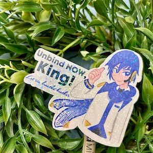Puede incluir: Una pegatina brillante con un personaje de estilo anime en azul y blanco con el texto "Unbind NOW, King!" y "Let em breathe brother." La pegatina est&aacute; sobre un fondo de follaje verde.