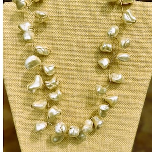 May include: A handcrafted necklace featuring irregularly shaped, off-white pearls strung on delicate gold-colored wire. The pearls are clustered together, creating a unique and elegant design. The necklace is displayed on a neutral-toned mannequin.