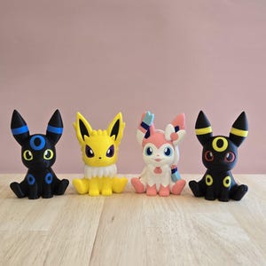 Può includere: Quattro piccole figurine di Pokemon. Un Umbreon nero e blu, un Espeon giallo, un Sylveon rosa e un altro Umbreon nero e blu.