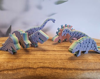 May include: Five colorful, articulated dinosaur toys made of plastic. The dinosaurs are in various poses and are a mix of green, blue, and pink.