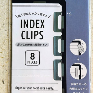 Op de afbeelding: Een verpakking met acht zilveren indexclips voor het organiseren van notitieboekjes. De verpakking bevat Japanse tekst die "Index Clips" en "8 Pieces" luidt. De tekst op de verpakking luidt ook "Organiseer uw notitieboekjes netjes. De indexclips passen perfect in de omslag."
