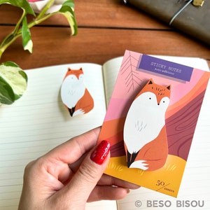 May include: A set of fox-shaped sticky notes with a matching design on the packaging. The notes are orange, white, and black, with the words "STICKY NOTES notes adhesives" printed on the top. The packaging has a colorful forest scene.