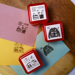 May include: Red square stamps with white illustrations and text, including "Have a Good Time!", "Nice Day!", and "Things to Do". The stamps are on colorful paper with matching stamped images.