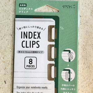 May include: A pack of 8 gold index clips for notebooks. The packaging is green and white with Japanese text that reads "Index Clips" and "Metal". The text "Organize your notebooks neatly" is also printed on the packaging.