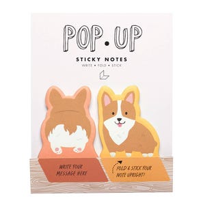 May include: Pop-up sticky notes featuring corgi dog designs. The notes are in the shape of a corgi, with one showing the rear and the other the front. Text on the packaging reads "Write Your Message Here" and "Fold & Stick Your Note Upright!"