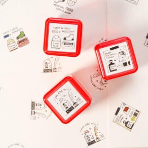 May include: Red square stamps with white inserts featuring black illustrations and text. One stamp reads "Have a Nice Holiday!" with drawings of a boot and cinema ticket. Another says "Enjoy the Small Things".