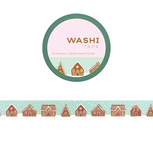 May include: Washi tape roll with a green border and a pink center that reads "Washi Tape". The tape features a repeating pattern of gingerbread houses on a light blue background. The text "10 meters - home sweet home" is also included.