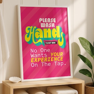 以下が含まれることがあります： ピンクと白のストライプの背景に「PLEASE WASH HANDS」と「Hands」の文字がレトロなスタイルで描かれた額入りのポスター。ポスターにはユーモラスなメッセージも含まれています。丸められたタオルが置かれた木製の棚の上に飾られています。