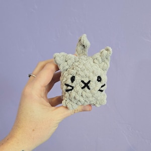 May include: A gray crocheted cat toy with black embroidered eyes and whiskers.