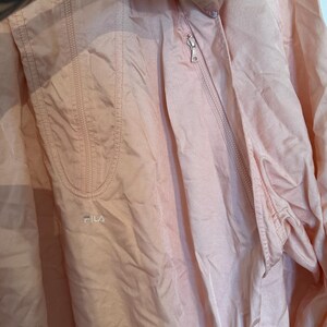 Puede incluir: Chaqueta cortavientos Fila rosa claro con cremallera. La chaqueta tiene un peque&ntilde;o logotipo de Fila en la parte delantera y un bolsillo en el lado izquierdo. La tela tiene un ligero brillo.