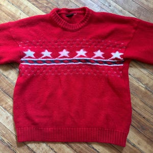 Peut inclure: Pull en tricot rouge avec un motif d'étoiles blanches et noires.
