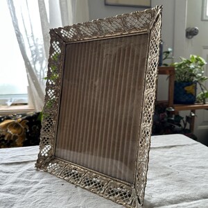 Peut inclure: Un cadre photo en métal argenté avec un design orné. Le cadre a une face en verre et un dos brun.