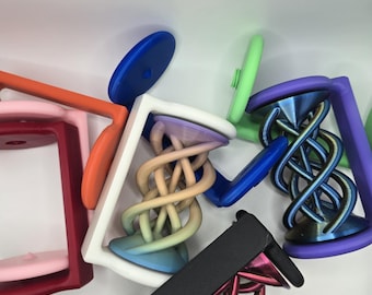 May include: A collection of colorful, 3D-printed objects with a unique, geometric design. The objects feature a square frame with a central, intertwined spiral element. Colors include pink, orange, blue, green, purple, and black.