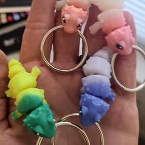 Pode incluir: Quatro chaveiros de lagarto segmentados e coloridos com argolas de chave prateadas. Os lagartos são rosa, azul, verde e amarelo.