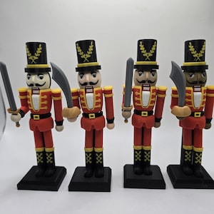 May include: Four wooden nutcracker soldiers in red uniforms with black boots and hats. Each figure holds a silver sword and stands on a black base. The hats are decorated with gold accents.