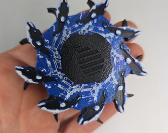 May include: A circular, blue and black decorative object featuring several orca whale figures. The whales are black and white, and the object has a textured, black center. The design is reminiscent of a water scene.