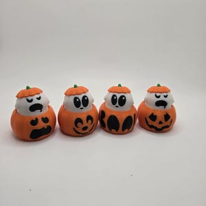 Pode incluir: Quatro pequenas figuras de abóbora de Halloween laranja e branca com diferentes expressões faciais. As abóboras são decoradas com olhos pretos, bocas e uma inscrição "BOO".