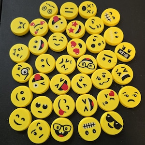 May include: A collection of 30 yellow emoji eraser toppers with various facial expressions, including happy, sad, surprised, and angry. The erasers are round and have black outlines.