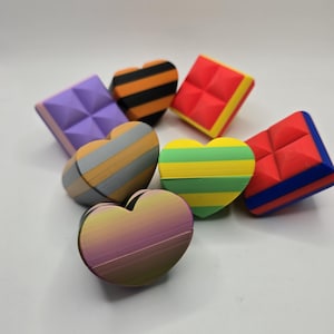 May include: A collection of colorful, heart-shaped and square-shaped objects. The hearts feature striped patterns in various colors, including yellow, green, orange, and gray. The squares have a geometric design and are in purple and red.