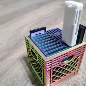 May include: A rainbow-colored plastic crate with a white memory card reader and a black SD card inside. The crate is designed to hold and organize small items.