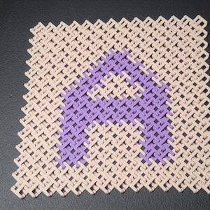 May include: A beige and purple cross-stitch pattern, featuring the letter "A" in a vibrant purple hue. The background is a light beige, creating a striking contrast. The design is a close-up shot, highlighting the texture and detail of the cross-stitch.