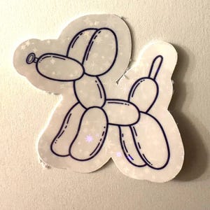 May include: A holographic sticker depicting a balloon dog. The dog's outline is dark blue, with details such as the eyes and tail. The sticker has a white background with a subtle glitter effect, creating a playful and whimsical look.
