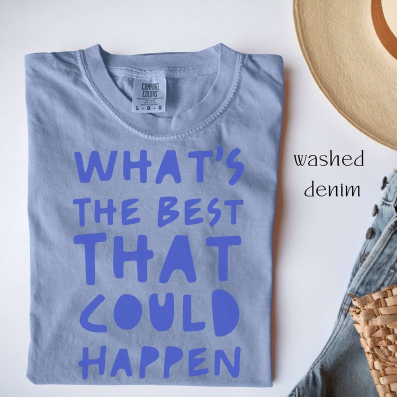 May include: A light blue t-shirt with the text "WHAT'S THE BEST THAT COULD HAPPEN" printed in blue. The shirt is folded and laid flat on a white surface.