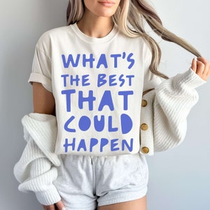 May include: A white t-shirt with the text "WHAT'S THE BEST THAT COULD HAPPEN" printed in blue.