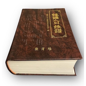 May include: A thick hardcover book with a textured dark brown cover featuring gold embossed Korean characters. The front cover displays a vertical title in a rectangular frame and additional text below. The pages are white and visible at the bottom.
