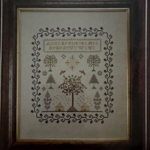 May include: Framed cross-stitch sampler with a brown wooden frame. The sampler features a decorative border and a central design with trees, birds, and houses. The top of the sampler has the alphabet stitched in capital letters.