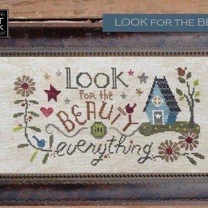 May include: Framed cross-stitch artwork with the text "Look for the Beauty in Everything." The design includes a blue house, flowers, stars, and hearts. The frame is dark brown.