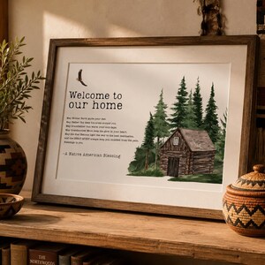 May include: A framed wall art print featuring a log cabin in a forest, a flying bird, and the text Welcome to our home followed by a Native American blessing. The print is housed in a dark wood frame with a white mat, displaying a nature-inspired scene.