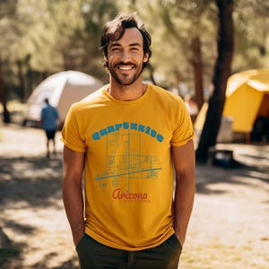 May include: A man wearing a yellow t-shirt with a blue and white graphic of a city map and the text "Surprise, Arizona" printed on it.