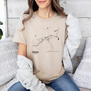 Peut inclure: Un t-shirt beige avec une carte en noir et blanc de Williams, en Arizona, imprimée sur le devant. Le texte "Williams, Arizona" et les coordonnées "35.2499° N, 112.1952° W" sont imprimés sous la carte.