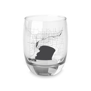 Puede incluir: Una copa de vino sin tallo transparente con un mapa en blanco y negro de Appleton, Wisconsin. El diseño del mapa incluye las calles, vías fluviales y un área sombreada que representa el contorno de la ciudad. La palabra "APPLETON" está impresa en negro.