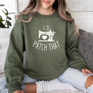 Puede incluir: Una sudadera verde con un gráfico blanco de una máquina de coser y el texto "I'd Patch That".