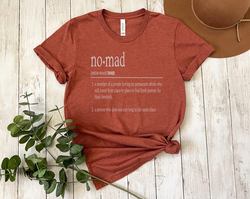 May include: A rust-colored t-shirt with the word "no-mad" defined as a person who does not stay long in the same place.