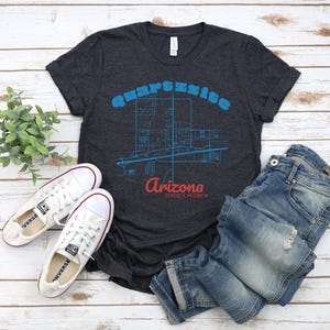May include: A dark heather grey t-shirt featuring a blue and white graphic of the city of Quartzsite, Arizona. The text "Quartzsite Arizona" is printed in blue and white on the shirt.