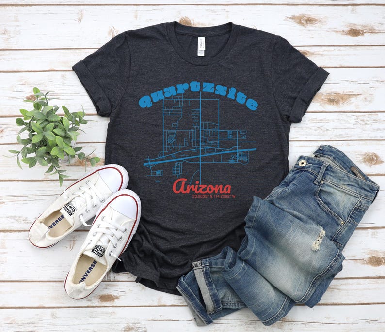 May include: A dark heather grey t-shirt featuring a blue and white graphic of the city of Quartzsite, Arizona. The text "Quartzsite Arizona" is printed in blue and white on the shirt.