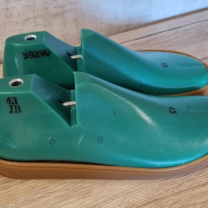 Könnte beinhalten: Zwei grüne Schuhleisten mit braunen Sohlen. Auf den Leisten sind die Nummern "43 JB" und "59290" aufgedruckt. Diese Schuhformen bestehen aus einem festen Material und dienen zur Formgebung von Schuhen. Größe 43, entspricht ca. 27 cm.