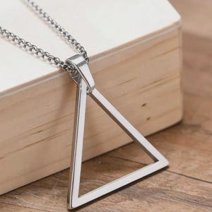May include: A silver-toned metal necklace featuring a hollow triangle pendant suspended from a matching link chain. The pendant is a simple geometric shape with a polished finish, attached to the chain by a small, integrated metal bail.