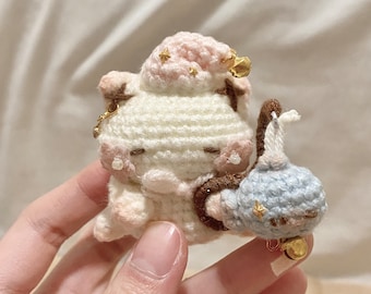 May include: Two crocheted amigurumi toys, one white with a pink hat and gold bells, the other blue with gold stars, holding hands.