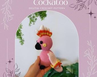Op de afbeelding: Een roze gehaakte Major Mitchell's Kaketoe vogel met een zwarte snavel en een kleurrijke kuif. De tekst "Major Mitchells Cockatoo DIGITAL CROCHET PATTERN" staat boven de vogel. De vogel wordt in een hand gehouden.