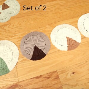 May include: A set of two or more handmade, circular coasters. The coasters are made of a cream-colored, woven material with a pie-shaped section in various colors, including brown, green, and tan. The text "Set of 2" is visible.